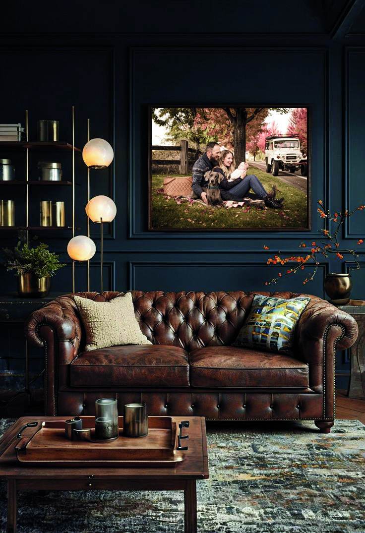 A framed portrait in a dark panelled study with a leather chesterfield